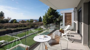 Uma varanda com barreira de vidro, piscina, cadeiras de descanso e uma mesa.