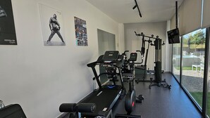 A gym with exercise equipment, posters on the wall, and a view of a swimming pool outside.