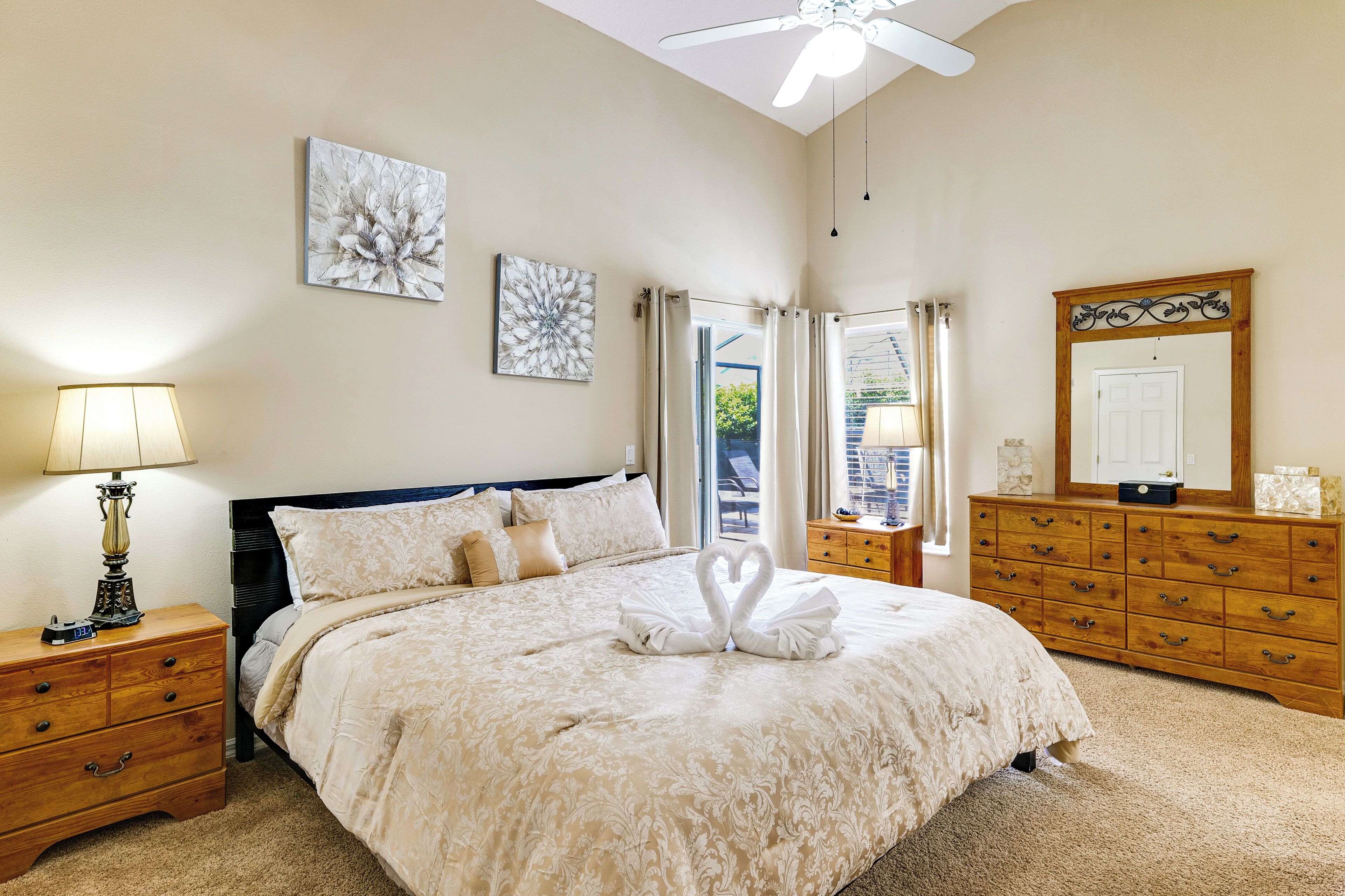 A hotel room with a bed, a nightstand with a lamp, a dresser, a mirror, and artwork on the walls.