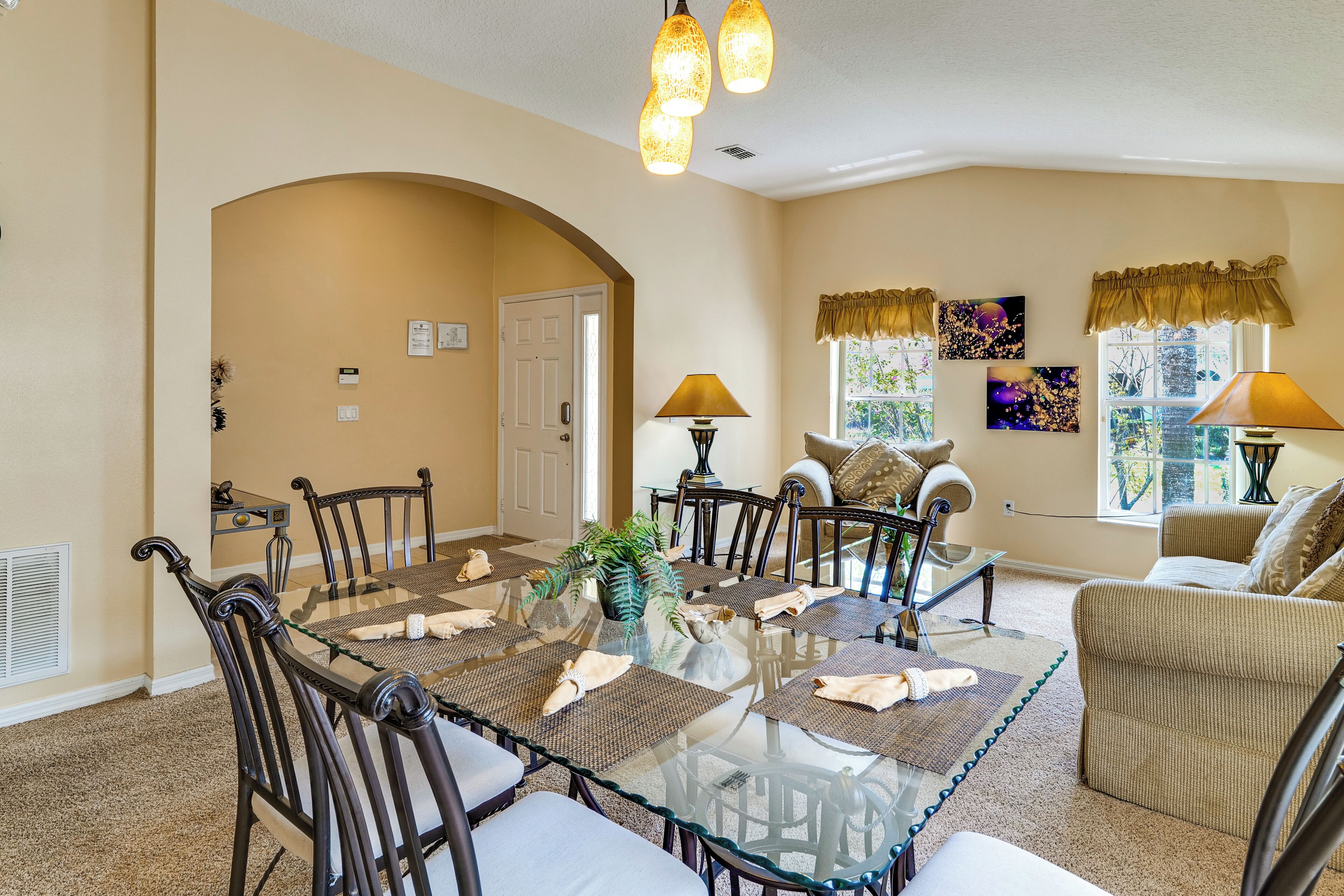 A dining area with a glass table surrounded by chairs, a sofa, and two lamps.