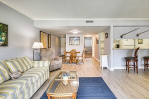 A living room with a striped sofa, a glass coffee table, a wooden dining table with chairs, and a kitchen area with a refrigerator and a microwave. - Boat Dock, Slips & Pool! St Johns River Condo (Welaka)