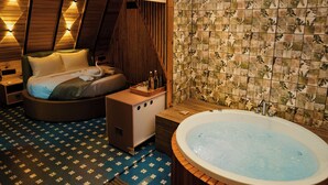 Una habitación con cama, un banco de madera, un jacuzzi y una pared con baldosas estampadas.
