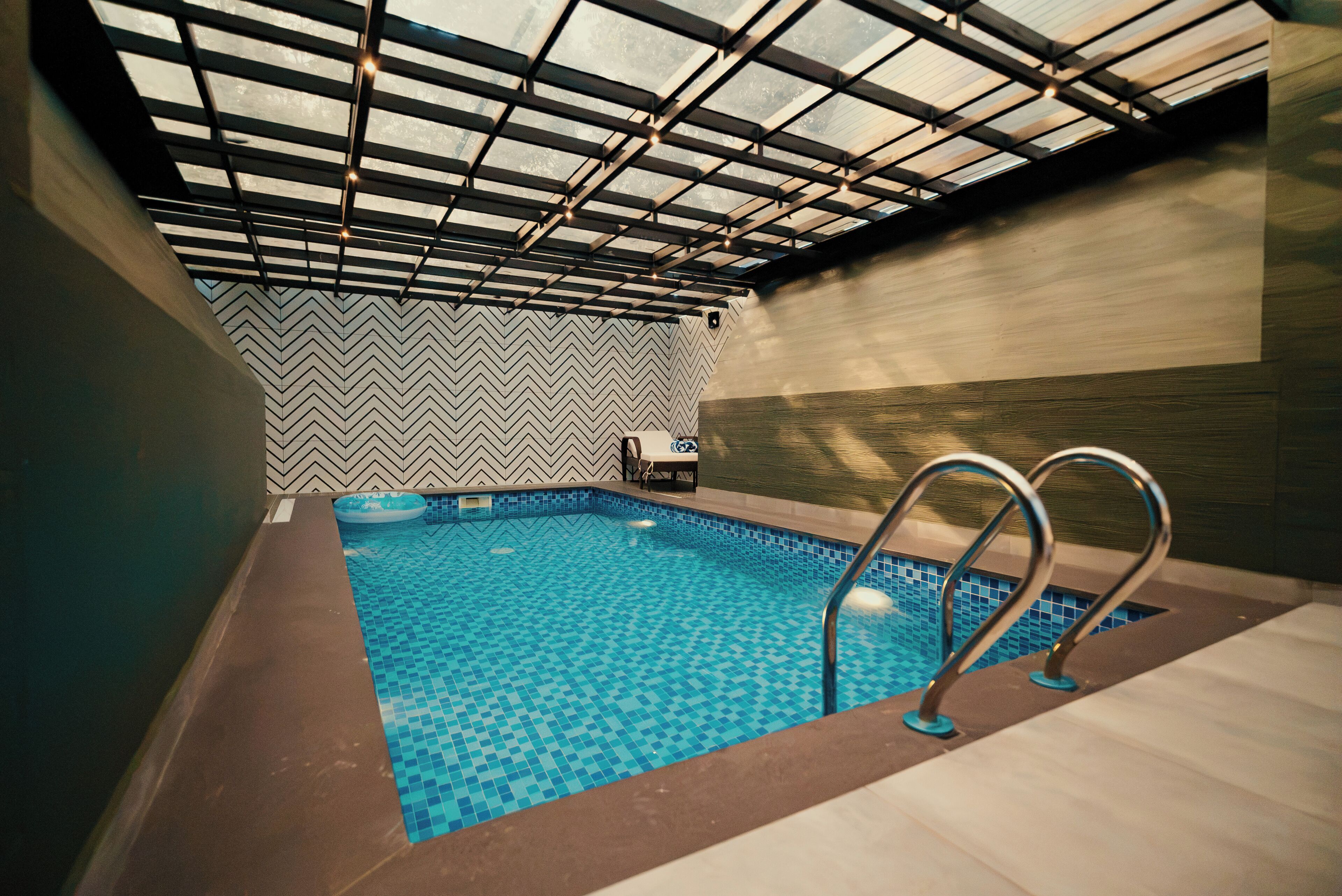 An indoor swimming pool with a chevron-patterned wall, a glass ceiling, and a wooden floor.