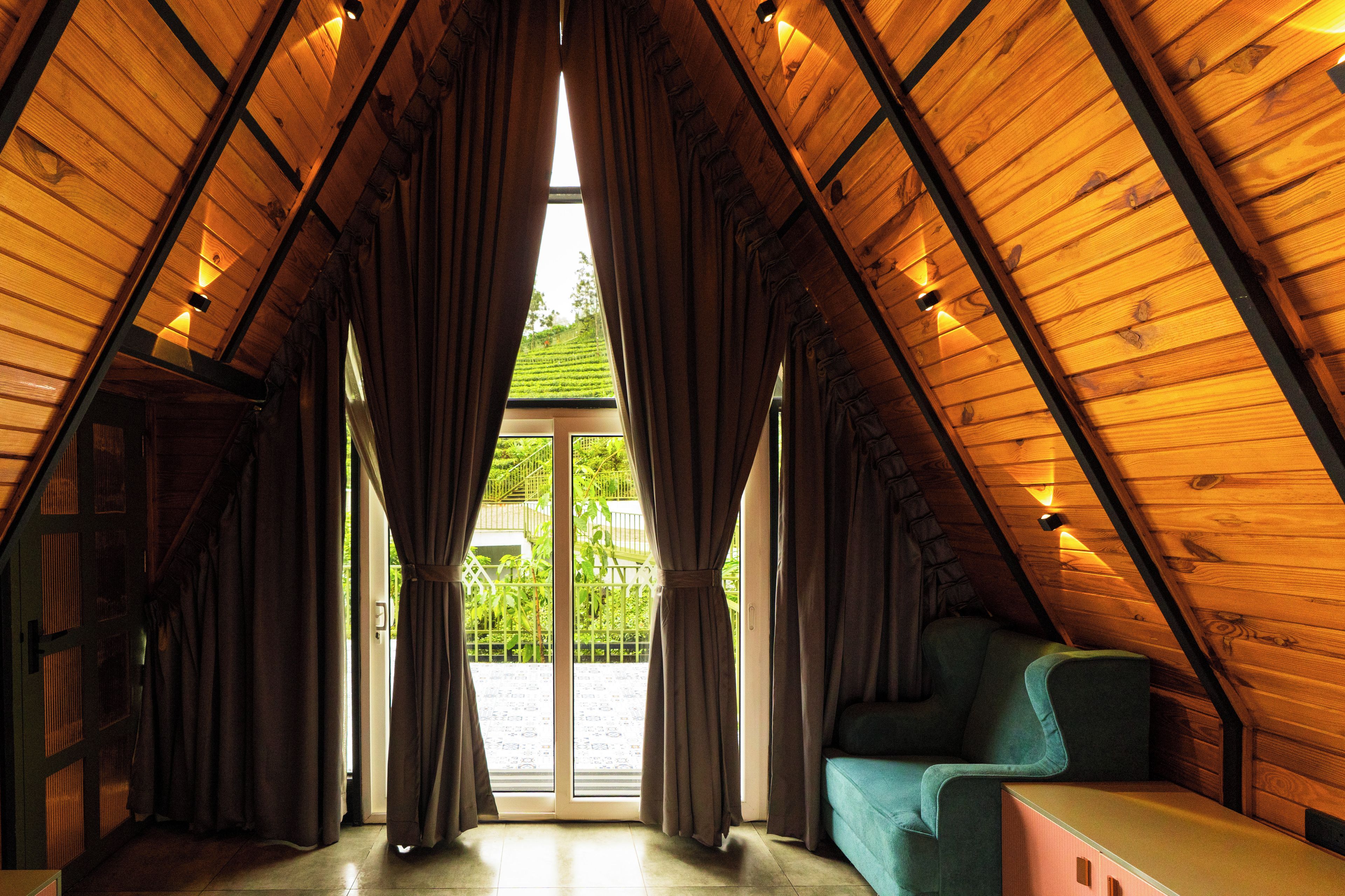 A room with a sloped ceiling, a large window with curtains, a sofa, and a small table.