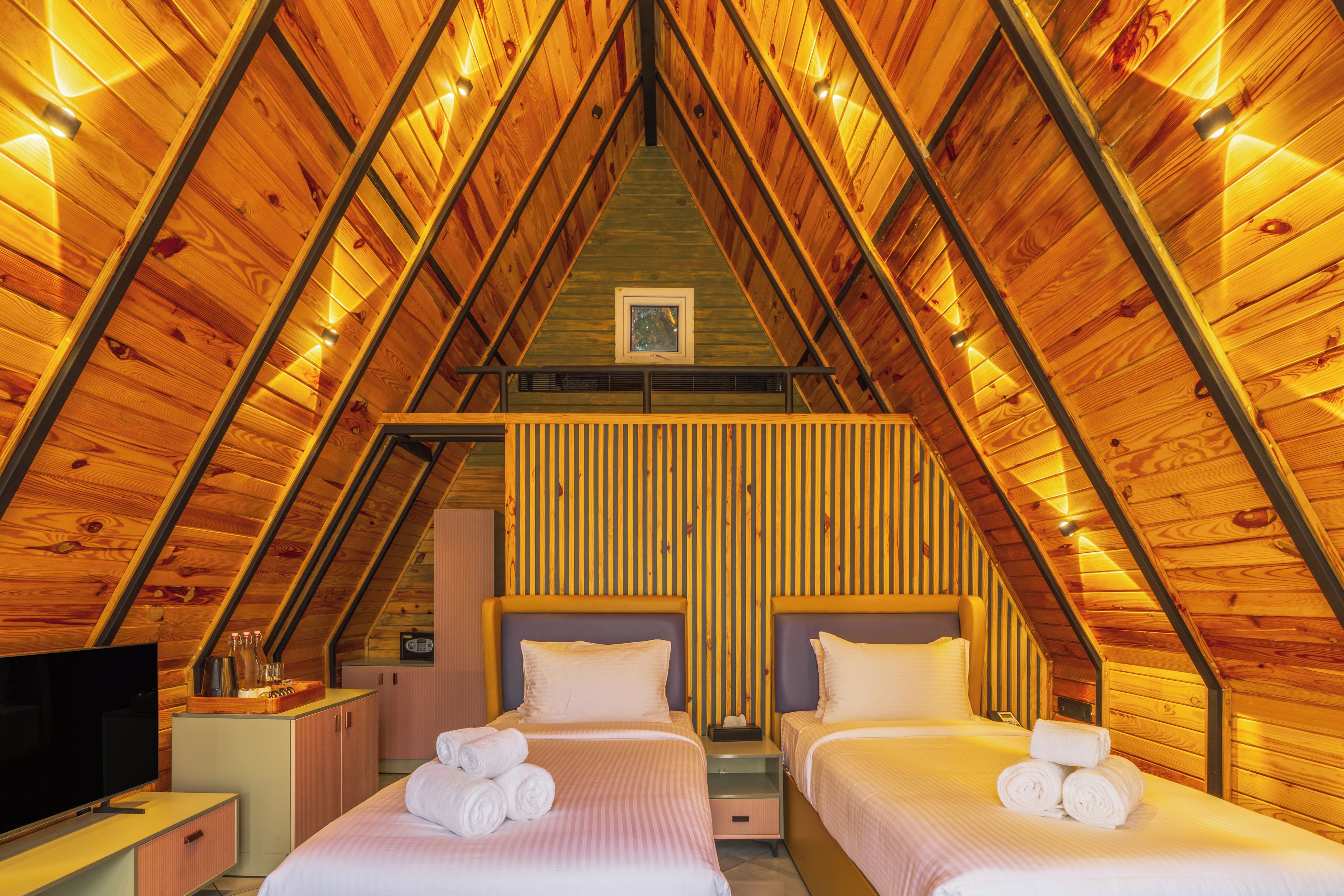 A room with two beds, a television, and a wooden ceiling structure.