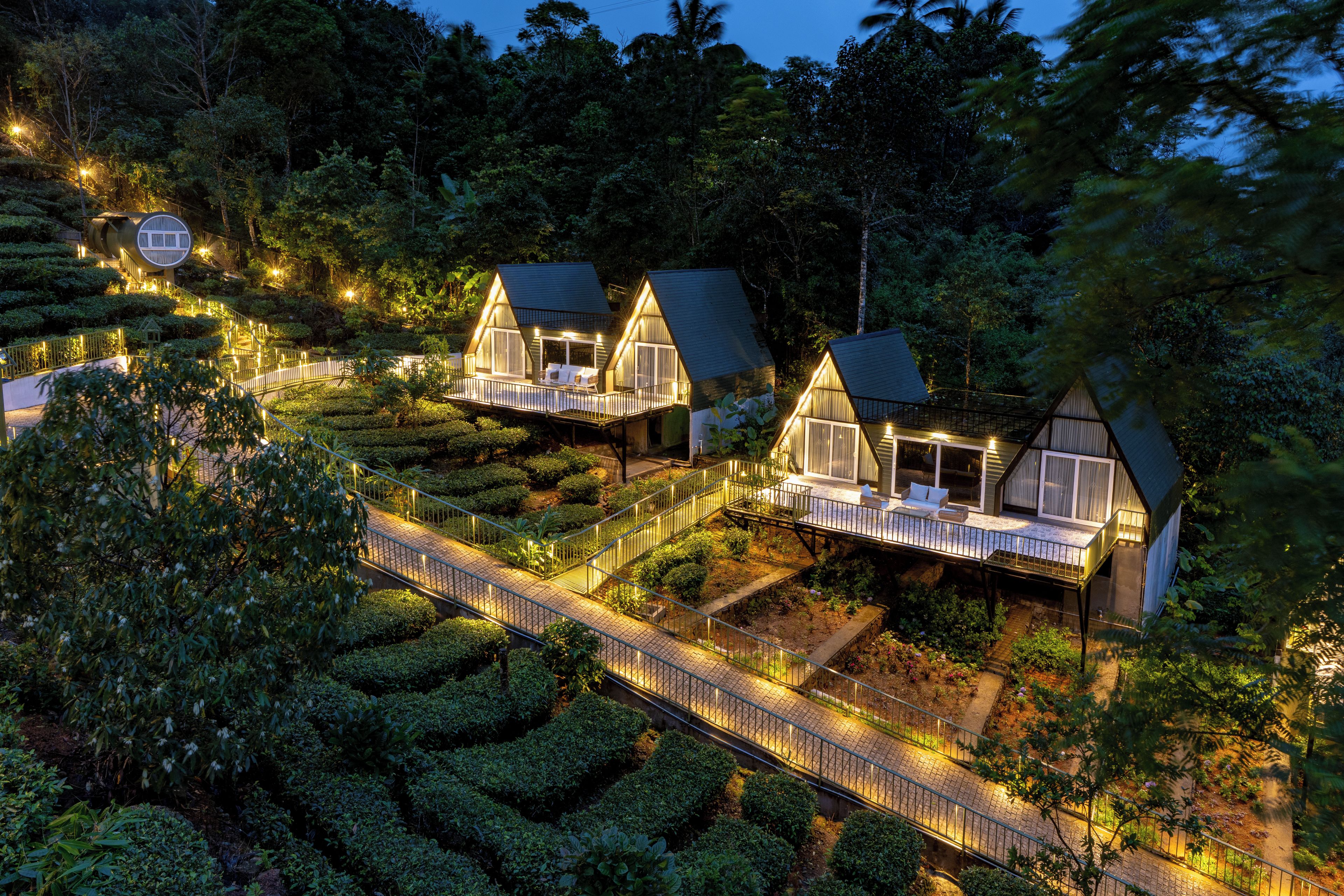 Une série de cabanes dotées de toits triangulaires et d’espaces extérieurs aménagés pour s’asseoir, entourées de jardins en terrasses et d’un sentier sinueux.