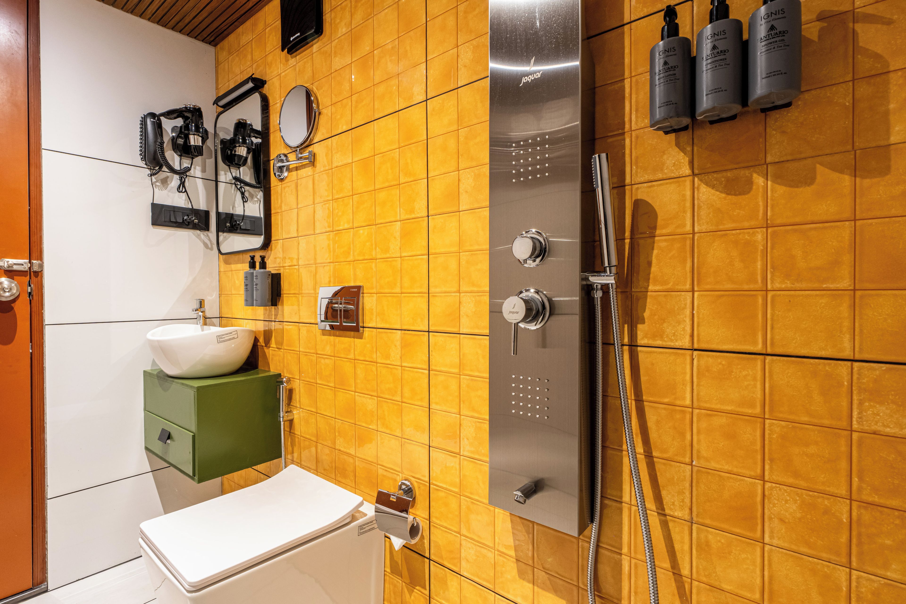 Un baño con pared de azulejos amarillos, un lavamanos blanco, un armario verde, un inodoro, un espejo y una ducha con cabezal de ducha manual.