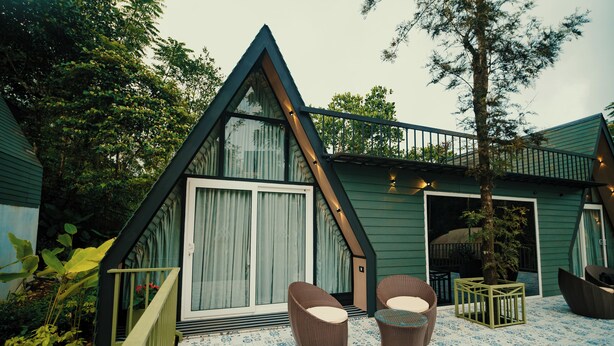 Un edificio de forma triangular con un amplio portón corredizo, dos sillas de mimbre y un suelo estampado.