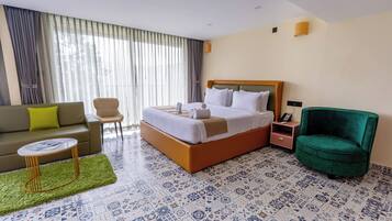 A hotel room with a bed, a sofa, a chair, a small table, and patterned floor tiles.