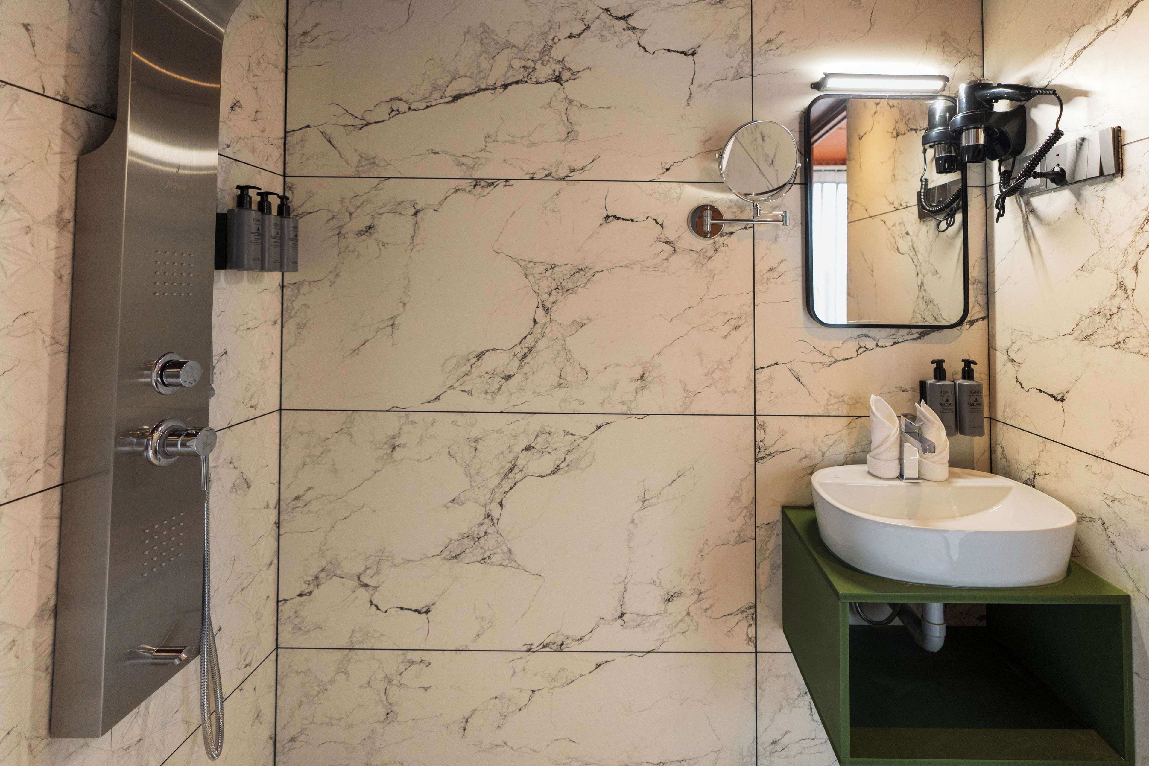 A bathroom with a marble wall, a shower, a sink with a green cabinet, and a mirror.