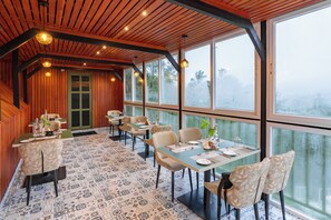 A restaurant with wooden ceiling beams, large windows, and patterned floor tiles.