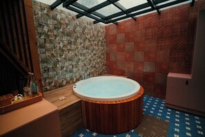 A bathroom with a wooden bathtub, a glass ceiling, and patterned tiles.