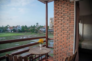 A balcony with a wooden table and chairs, a brick wall, and a view of a residential area with houses and greenery. - Laoxao River Homestay
A charming riverside hotel where natural beauty (Đà Nẵng)
