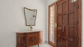 Una puerta de madera con un panel de vidrio, un aparador de madera con frente de mármol y cajones, y un espejo montado en la pared.