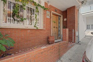 A brick building with a wooden door, a window with metal bars, and a potted plant on the ground. - Apartment 'El Olivo 2' with 2 Private Terraces, Wi-Fi, and Air Conditioning (Málaga)