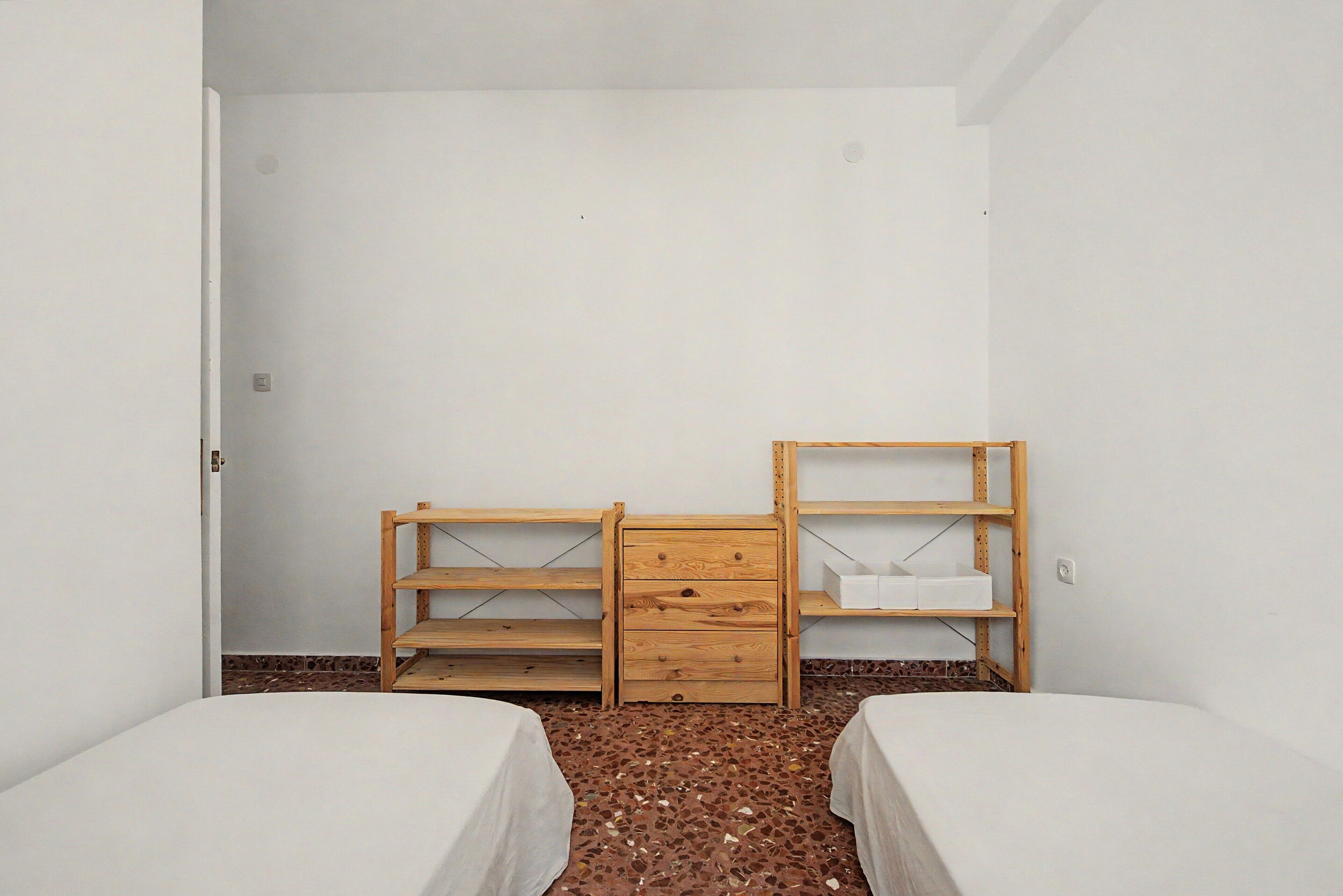 Ein Zimmer mit zwei Betten, einem Holzschrank und einem Regal.