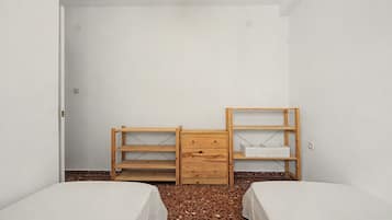 Ein Zimmer mit zwei Betten, einem Holzschrank und einem Regal.