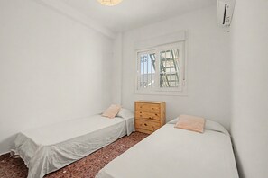 Ein kleines, sauberes Zimmer mit zwei Einzelbetten, einem Holzkoffer und einem Fenster mit Gitterstäben.