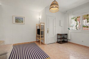 A room with a striped rug, a television on a wooden stand, a white door, a table, and a window with a view of buildings. - Apartment 'El Olivo 2' with 2 Private Terraces, Wi-Fi, and Air Conditioning (Málaga)