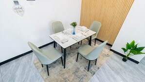 Un comedor con una mesa blanca dispuesta para cuatro, sillas de color gris claro, un florero azul con flores y una pared de listones de madera detrás de la mesa.