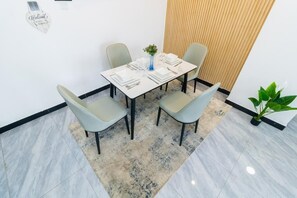 Ein Essbereich mit einem weißen Tisch, gedeckten Plätzen für vier Personen, hellgrauen Stühlen, einer blauen Vase mit Blumen und einer Wand mit Holzleisten im Hintergrund.