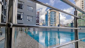 Una piscina con cubierta de piedra y barandillas de metal, rodeada de edificios modernos.