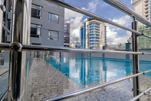 Ein Schwimmbecken mit einer Steindeck und Metallgeländern, umgeben von modernen Gebäuden.
