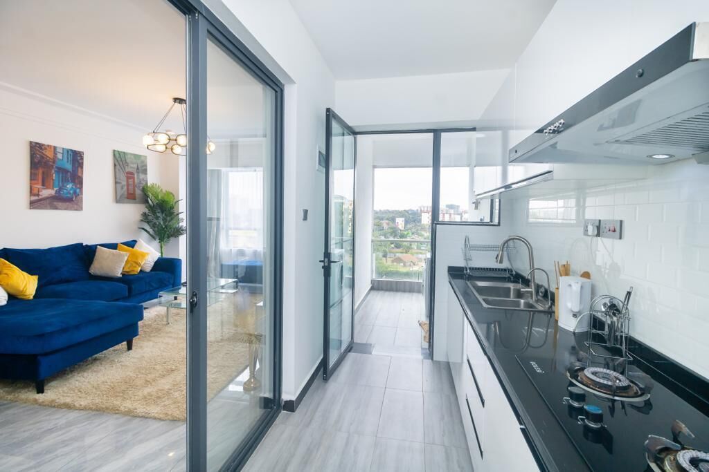 Une cuisine moderne avec un four noir, un évier en acier inoxydable et une vue sur la ville grâce à de grandes fenêtres.