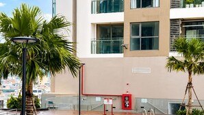 A modern building with a pool area, including a pool, palm trees, and a red fire extinguisher. - The Ruby Ha Long by LN Maison (cao xanh)