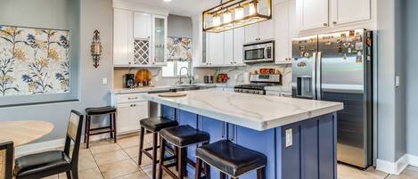 A modern kitchen with a large island, bar stools, a dining table, and a decorative wall piece.