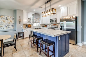 A modern kitchen with a large island, bar stools, a dining table, and a decorative wall piece. - Walk to Tucson Trails! Private Yard w/ Views (Tucson)