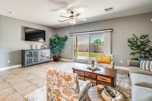 A spacious living room with a flat-screen TV, a ceiling fan, a large window with a view of the outdoors, and a dining area with a wooden table and chairs. - Walk to Tucson Trails! Private Yard w/ Views (Tucson)
