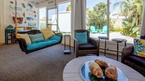 A room with a hanging chair, a sofa, and a dining table with coconuts. - Flip-Flop to Beach & Flagler Ave! Breezy Getaway (New Smyrna Beach)