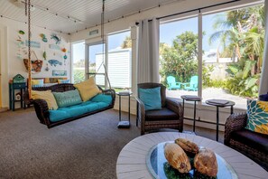 A room with a hanging chair, a sofa, and a dining table with coconuts. - Flip-Flop to Beach & Flagler Ave! Breezy Getaway (New Smyrna Beach)