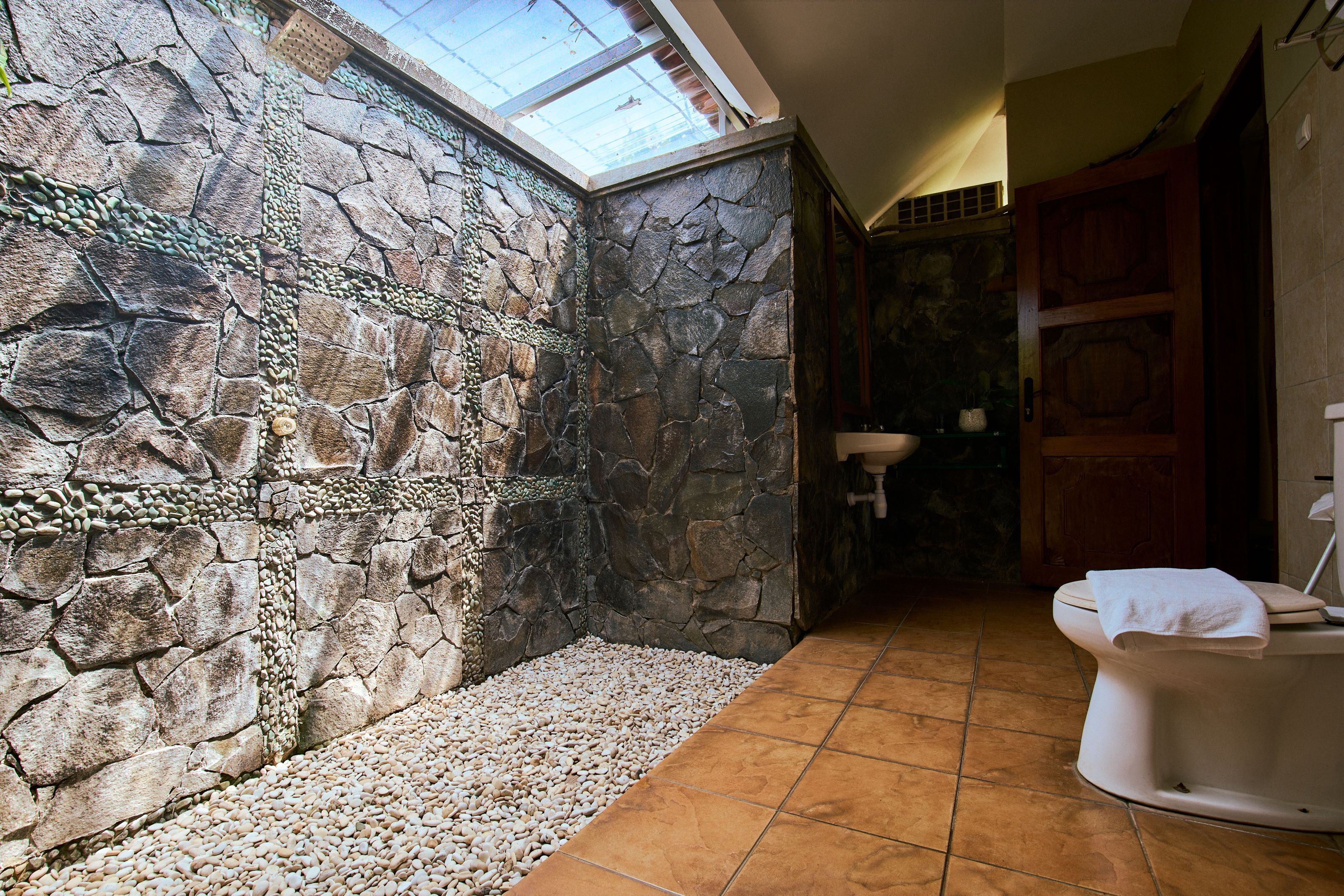A bathroom with a stone wall, a skylight, a toilet, and a sink.