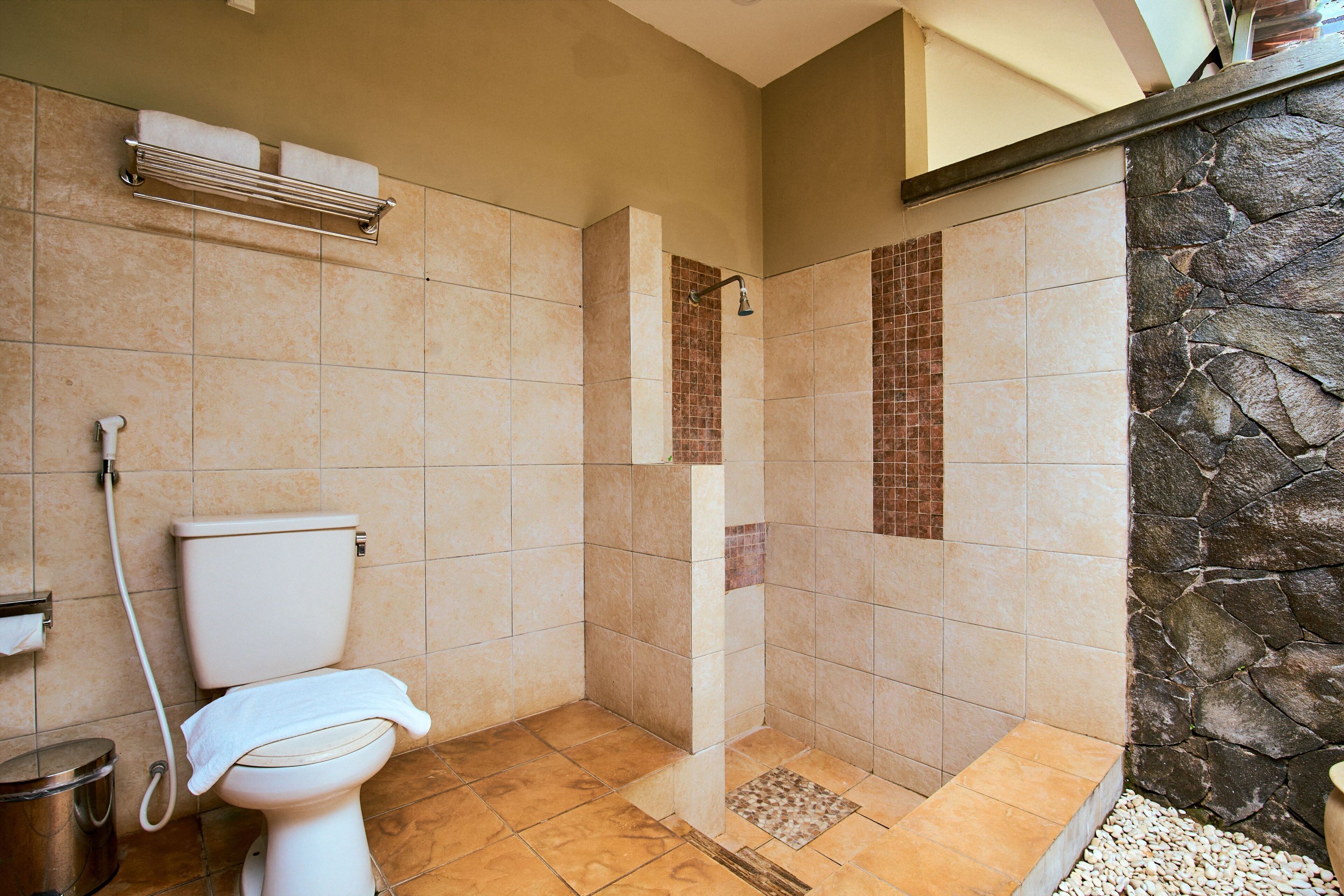 Un baño con inodoro, ducha y una pared de acento de piedra.