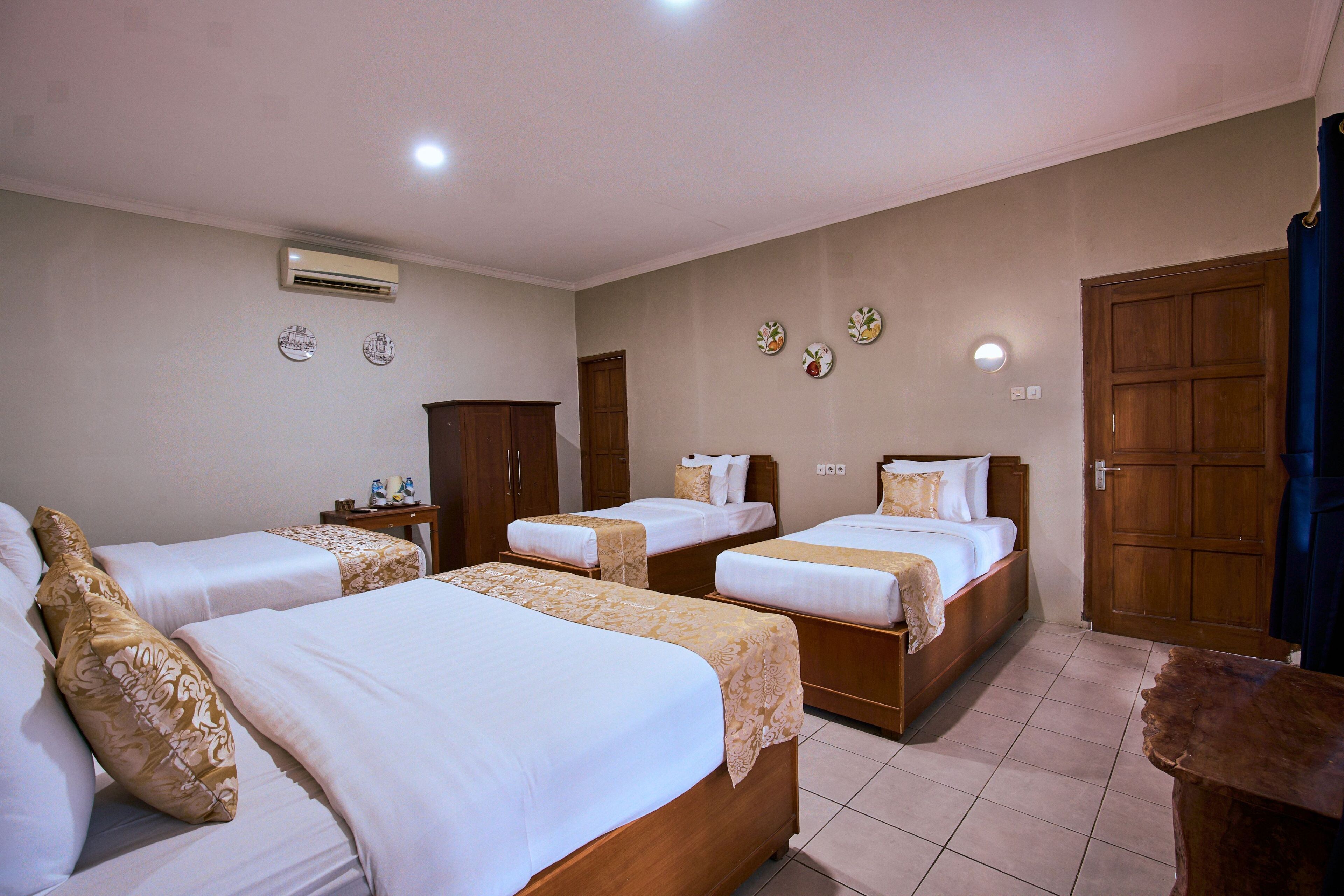 Habitación de hotel con cuatro camas individuales, un armario de madera, una mesita pequeña y un aire acondicionado instalado en la pared.