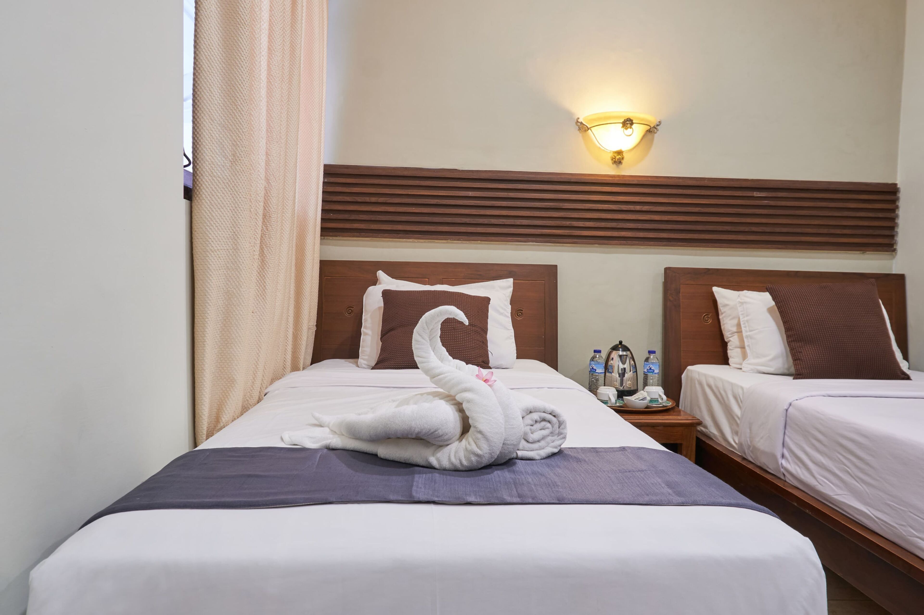 A hotel room with two beds, a nightstand with a lamp, and a window with curtains.