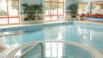 Una piscina con agua azul cristalina, rodeada de ventanas de marcos rojos y plantas de interior.
