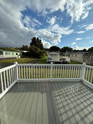 A deck with a white railing, a grassy area, and several mobile homes in the background.