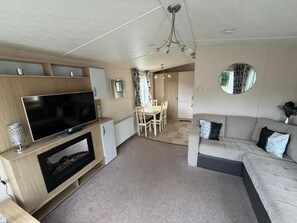 Un espacio habitable compacto con televisión de pantalla plana, un sofá, comedor y un espejo.