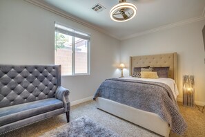 Une chambre à coucher avec un canapé capitonné, un lit recouvert d’une couvre-lit à motifs, une lampe de table et un grand lampadaire.