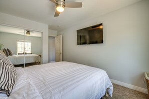 Quarto com cama, ventilador de teto, televisão de tela plana na parede e porta que dá para outro cômodo.