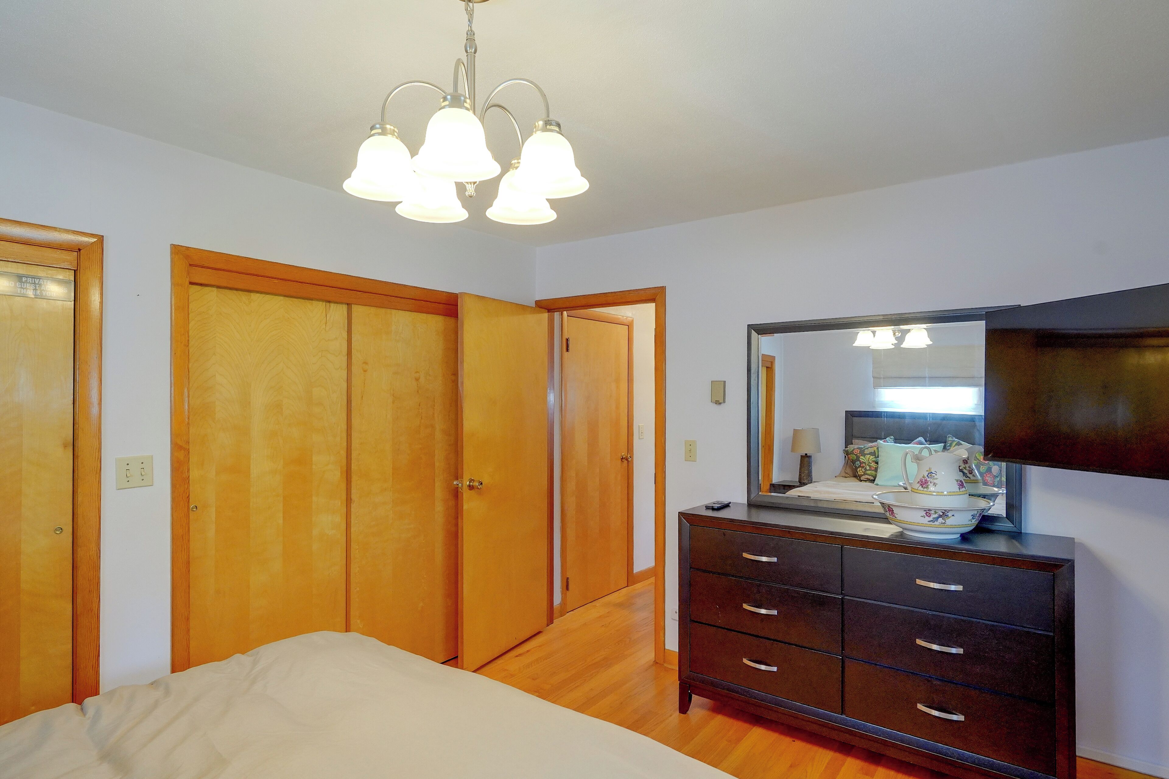 A bedroom with a bed, dresser, mirror, and two wooden doors.