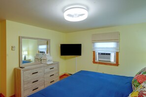 A bedroom with a bed, a dresser, a mirror, a flat-screen TV, and a window with blinds.