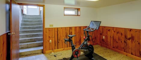 A room with a wooden floor, a Peloton exercise bike, a small window, and a staircase leading to another level.