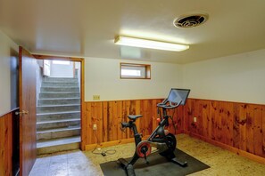 A room with a wooden floor, a Peloton exercise bike, a small window, and a staircase leading to another level.