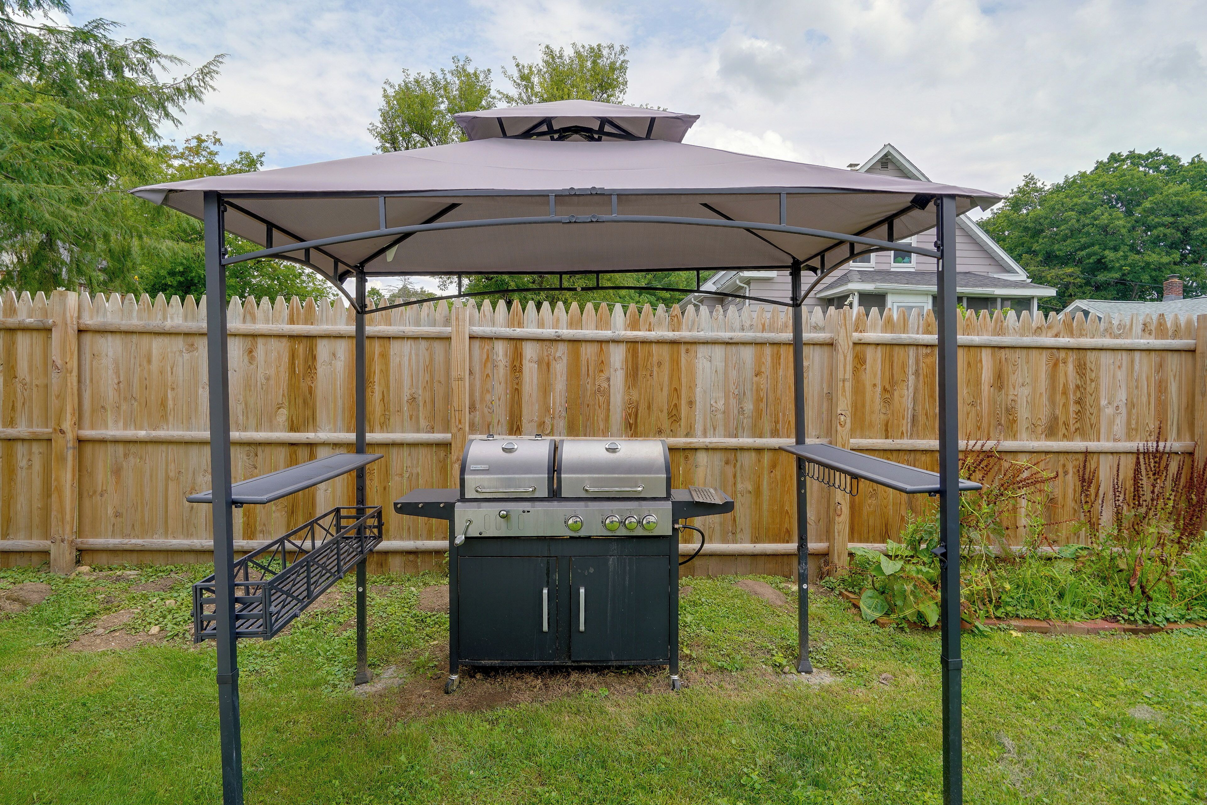 A barbecue grill under a covered pavilion with a wooden fence in the background.