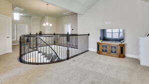 A spacious living area with a high ceiling, a staircase with a railing, and a television on a wooden cabinet. - Spacious Rowlett Home | Ideal for Extended Stays (Rowlett)