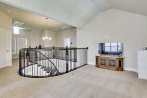 A spacious living area with a high ceiling, a staircase with a railing, and a television on a wooden cabinet. - Spacious Rowlett Home | Ideal for Extended Stays (Rowlett)